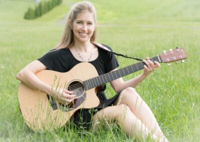 Stacy Gabel sitting in the grass with her guitar.