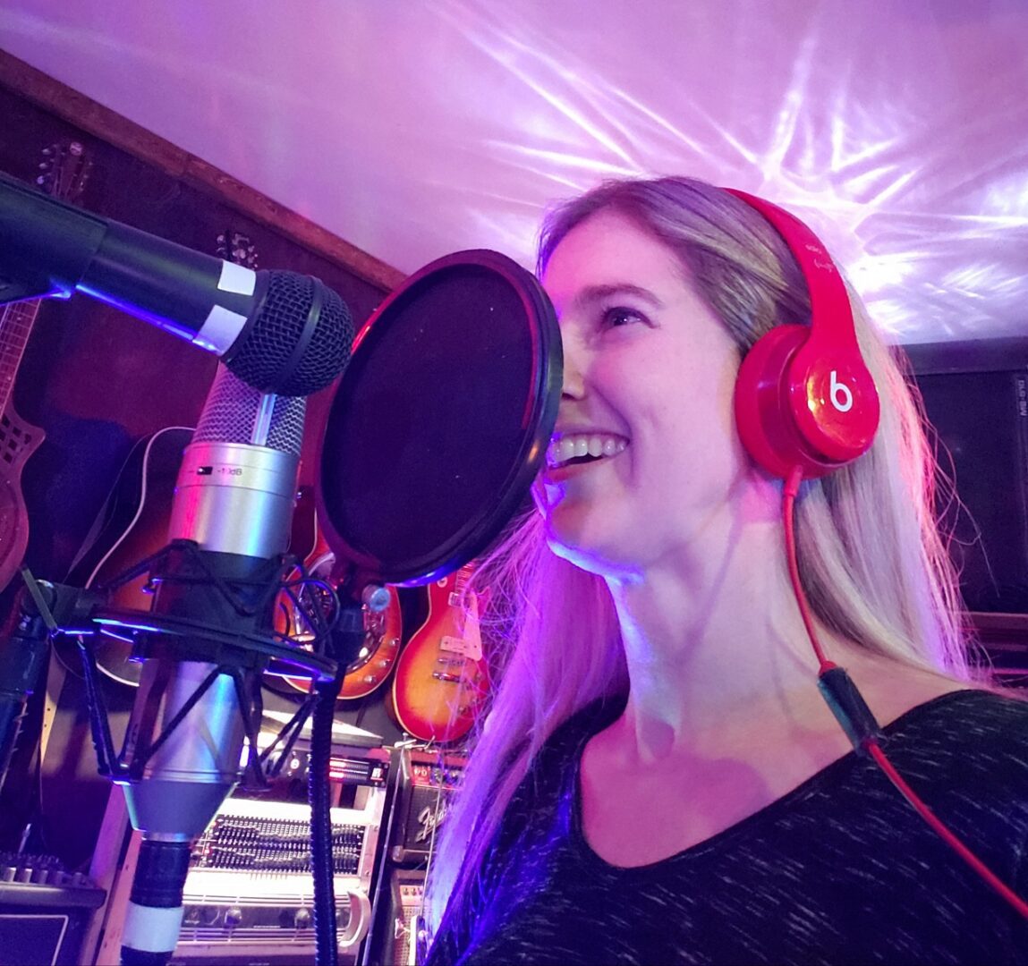 A woman with headphones on singing into a microphone.