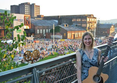 A woman standing on the side of a bridge with a guitar.
