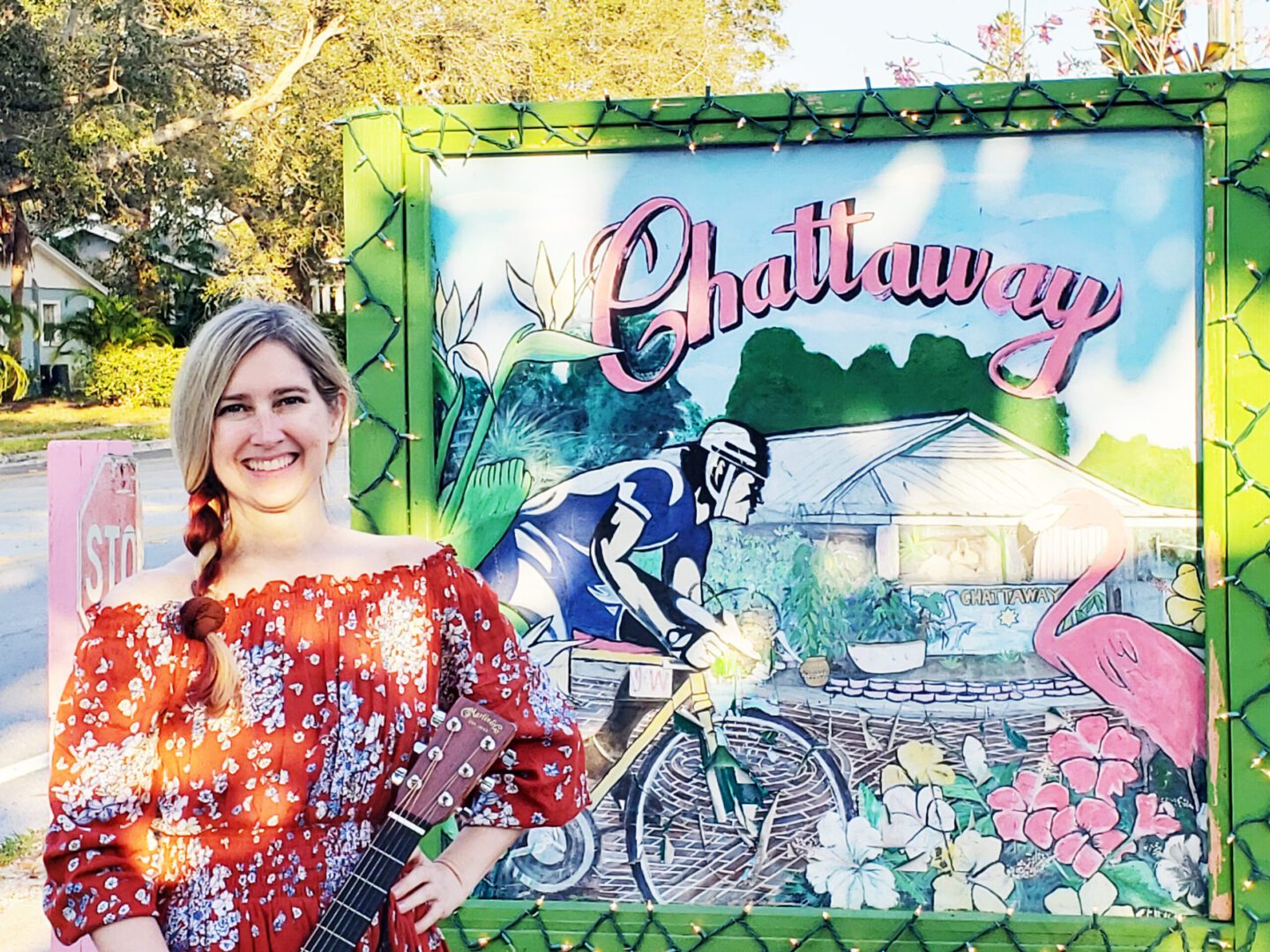 A woman standing in front of a sign with a guitar.